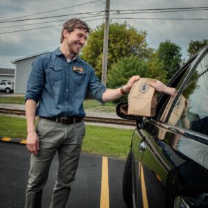 Kevin from Neighborhood Provisions delivers goods in a bag to a vehicle outside of the business